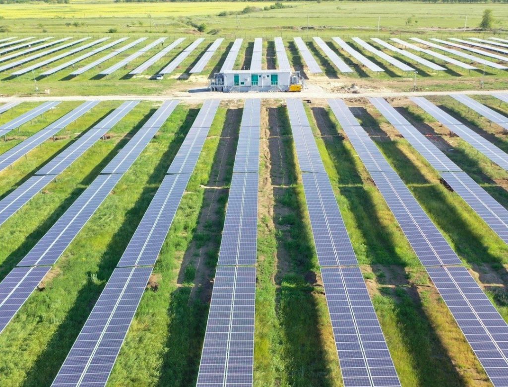Аэрофотосъемка аккуратных рядов солнечных панелей на зеленом поле — символ масштабной и эффективной солнечной электростанции.